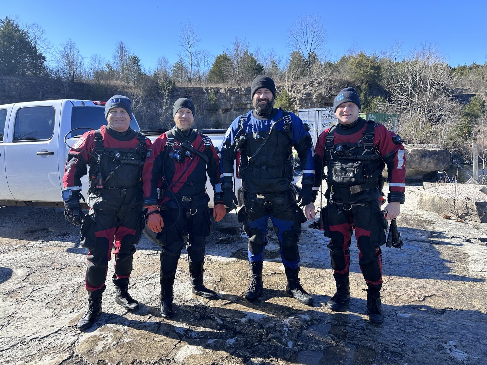 Four drysuit divers geared up beside a truck at the quarry